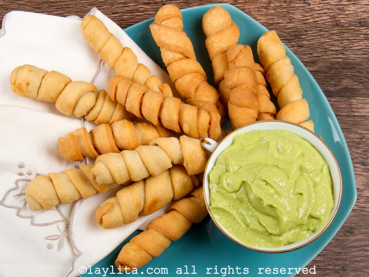 Tequeños served on a platter with a side of avocado dipping sauce