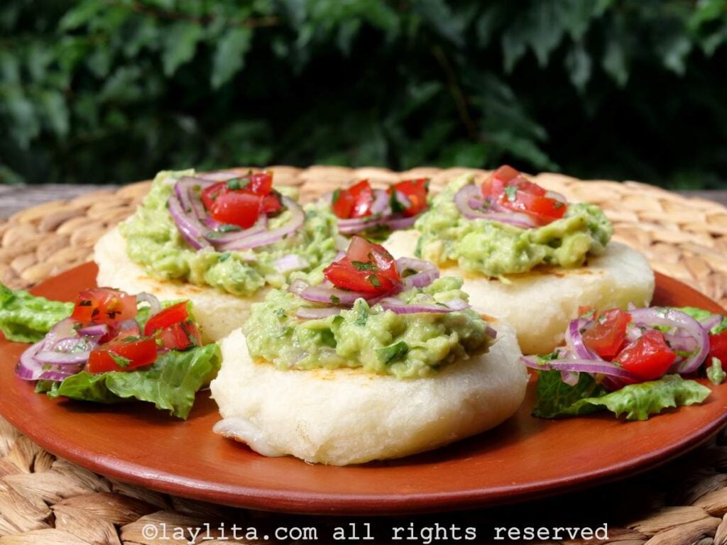 Three mashed yuca patties on a terracotta plate with avocado salsa on top