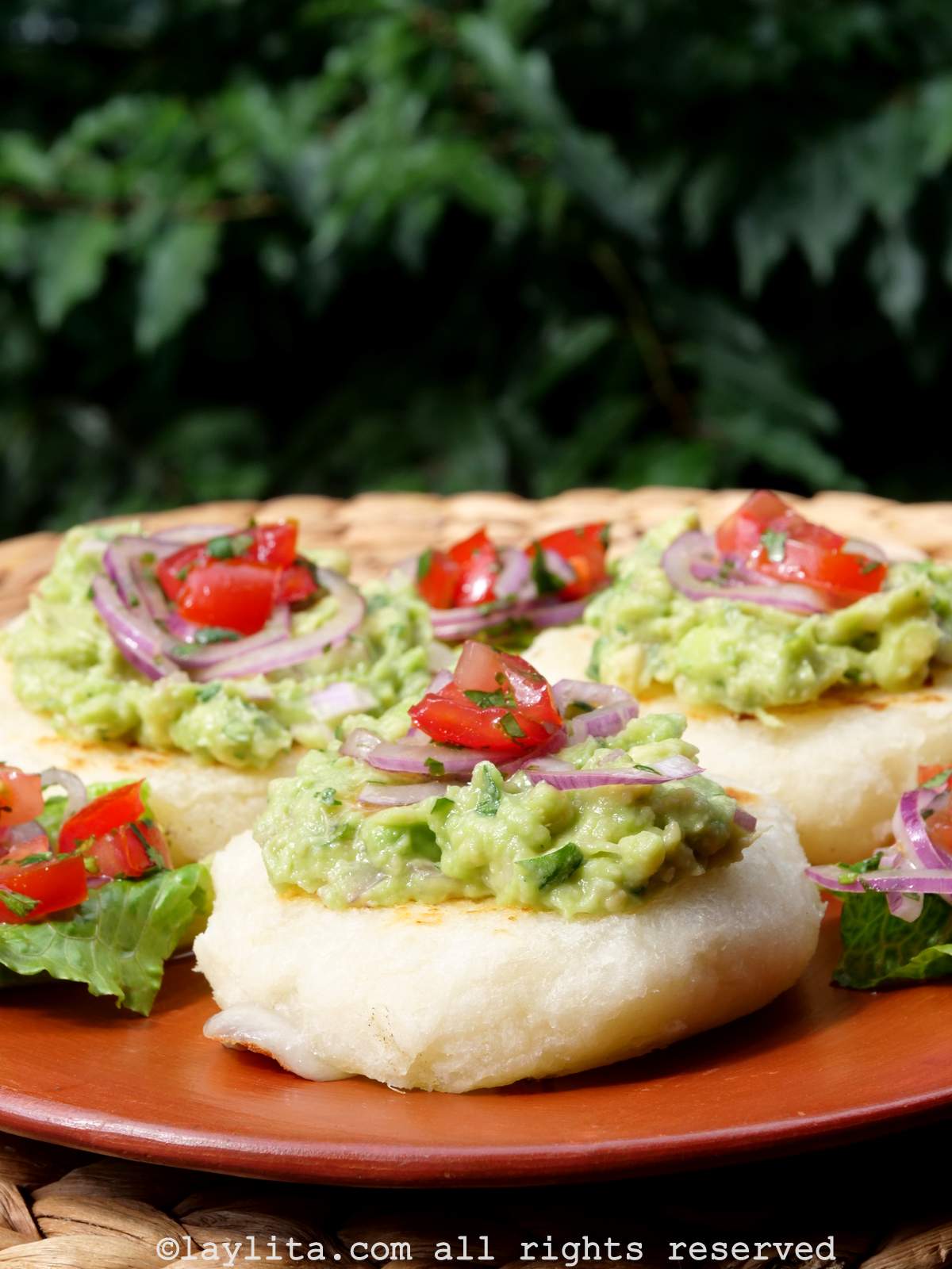 Side view of three Ecuadorian tortillas or llapingachos de yuca on a terracotta plate topped with mashed avocado and tomato