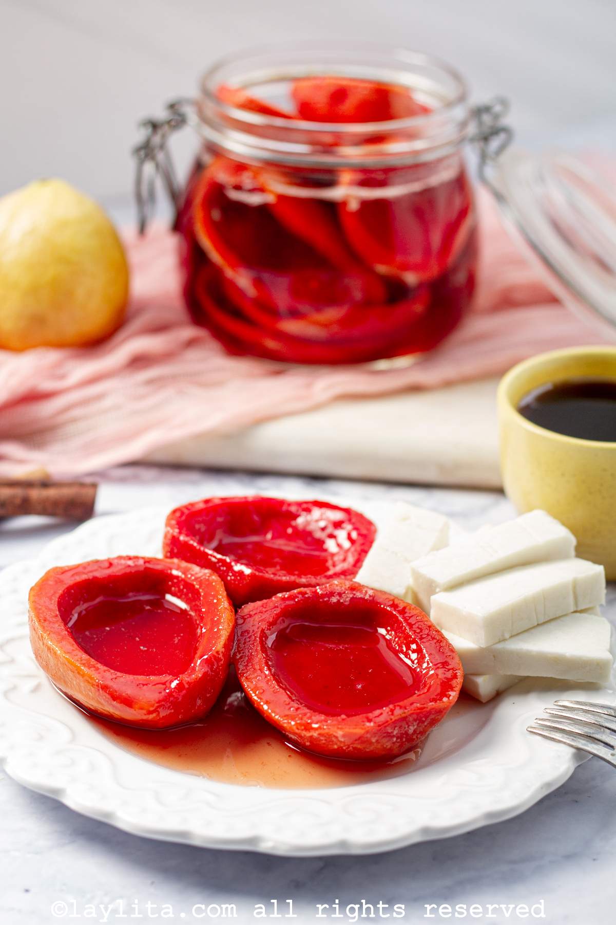 Three guava shells in syrup on a plate with cheese on the side, and more guavas in a jar in the background.