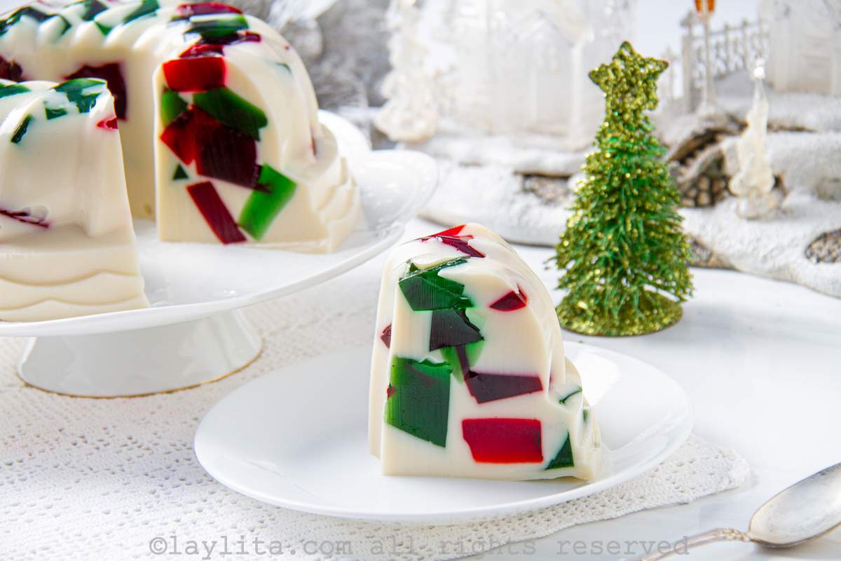Side view of a slice of mosaic jello on a plate next to the rest of the jello on a cake stand.