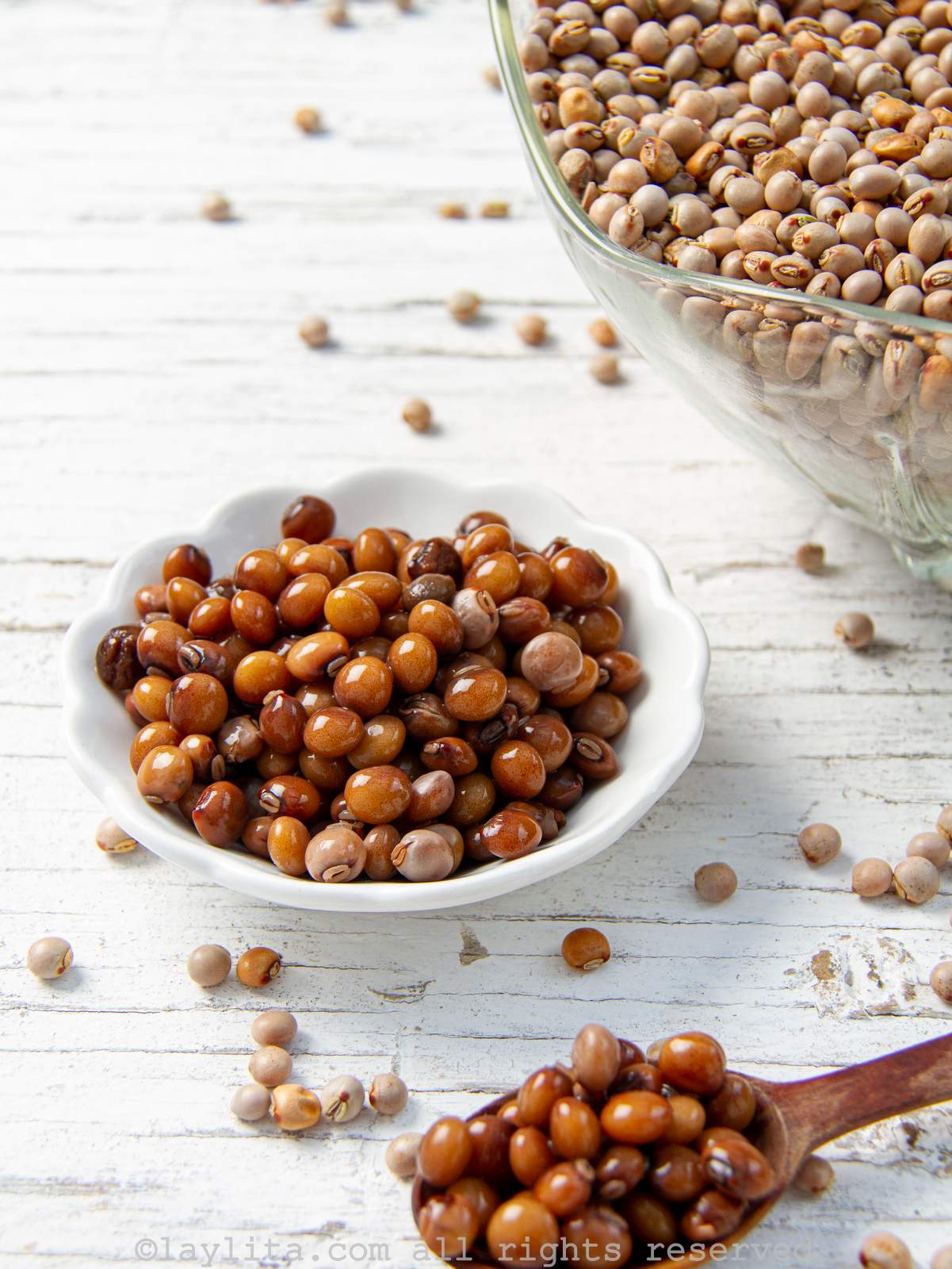 A small white bowl filled with cooked pigeon peas or gandules, with a spoon of them outside of the bowl. A glass bowl of dried pigeon peas is in the background.