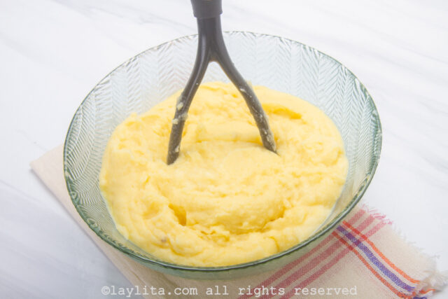Potatoes being mashed with a masher in a glass bowl