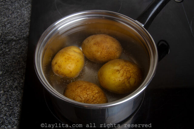 Four whole potatoes cooking in a pot of water