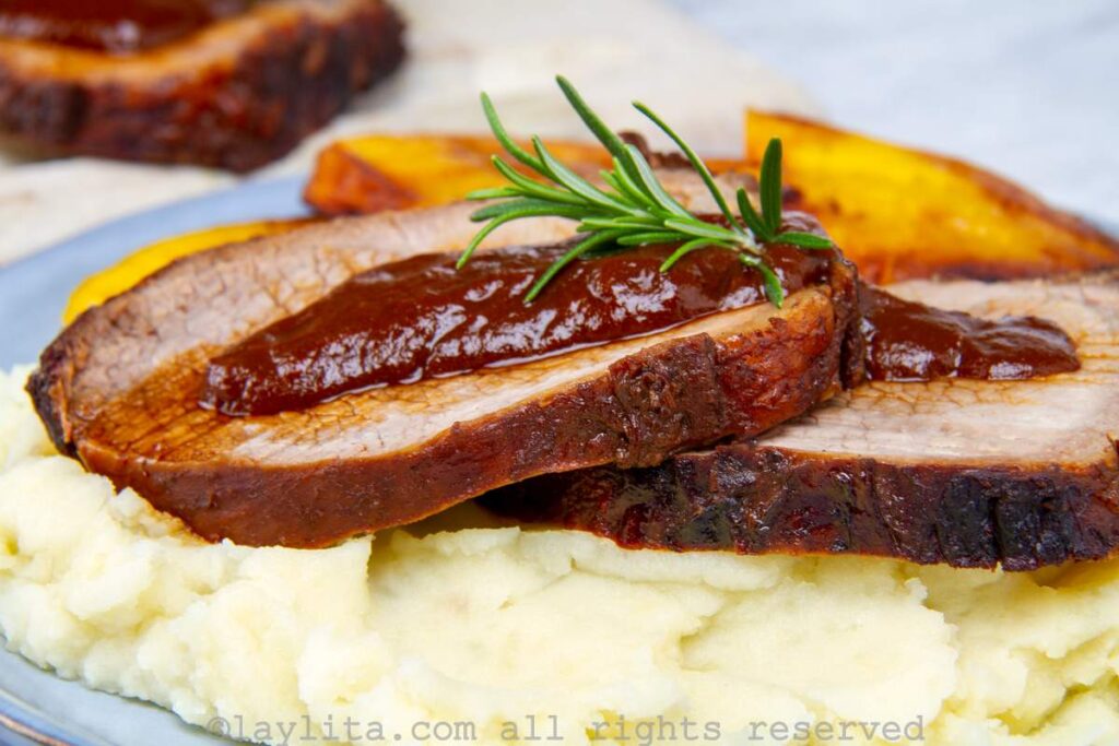 Venezuelan roasted beef served on a bed of mashed potatoes and a side of plantains with sauce on top.