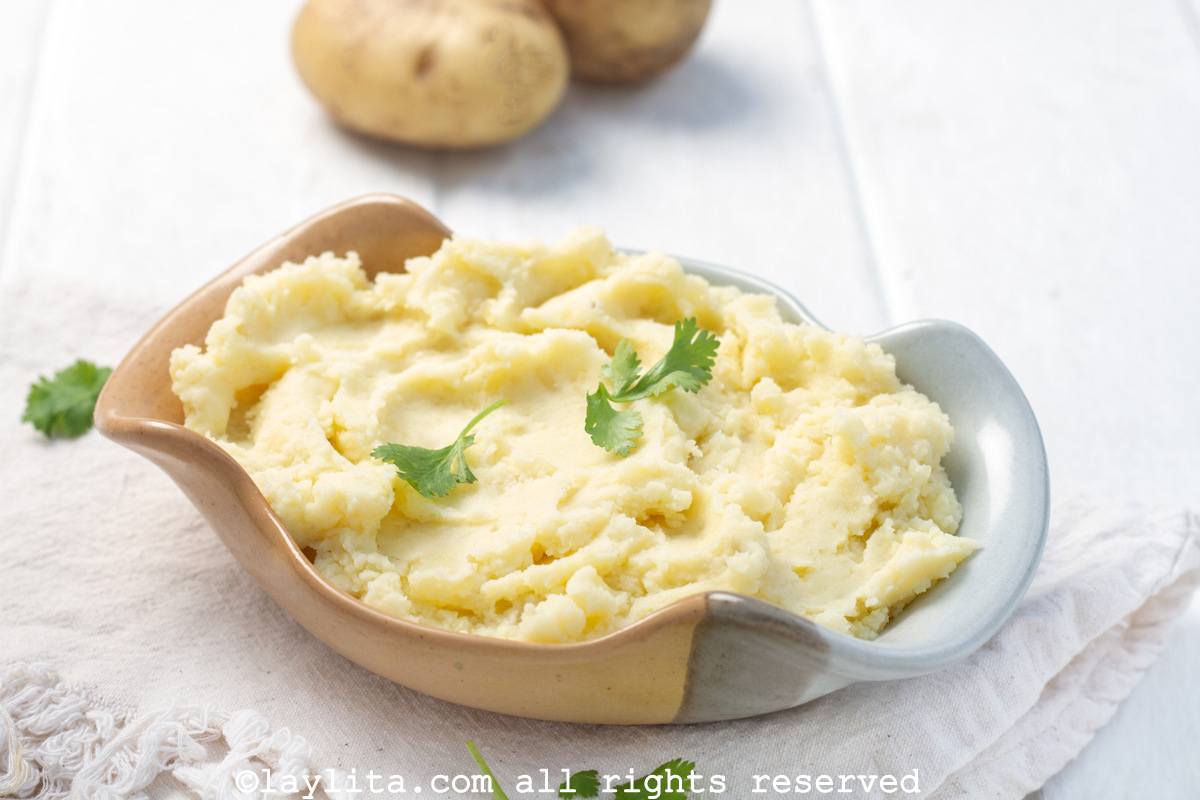 Serving bowl of rustic fluffy mashed potatoes with a sprig of parsley on top.