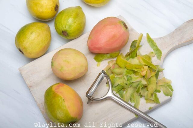 Guavas being peeled on a wooden cutting board.