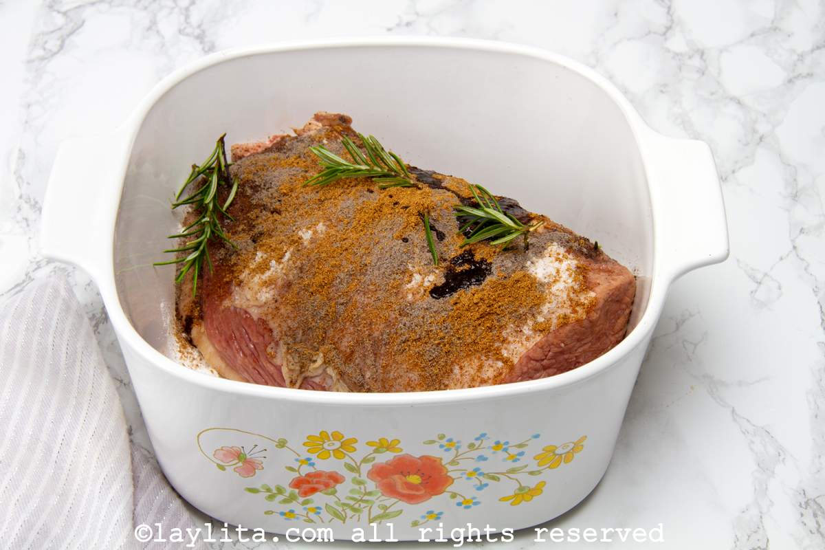 Eye of round roast covered in seasoning and rosemary in a dish.