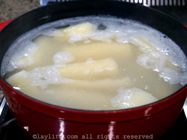 A red pot with boiling water and cassava pieces being cooked