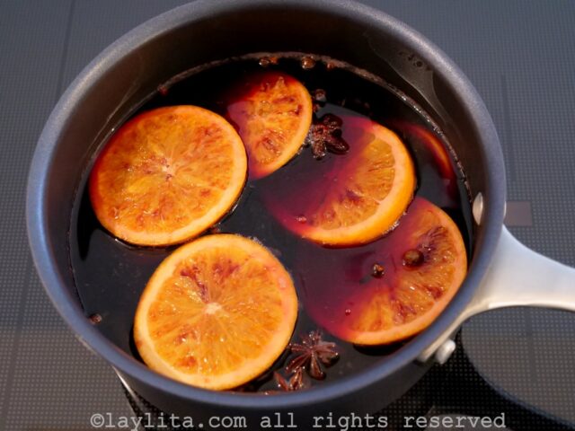 A pot of red wine, orange slices and spices simmering on the stove
