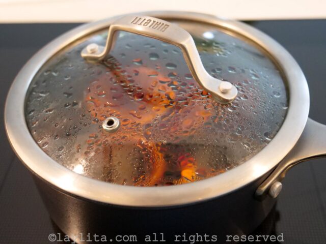 A pot with orange slices, spices and wine, covered with a lid, simmering on the stove