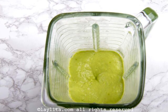 A blender with green avocado sauce being blended