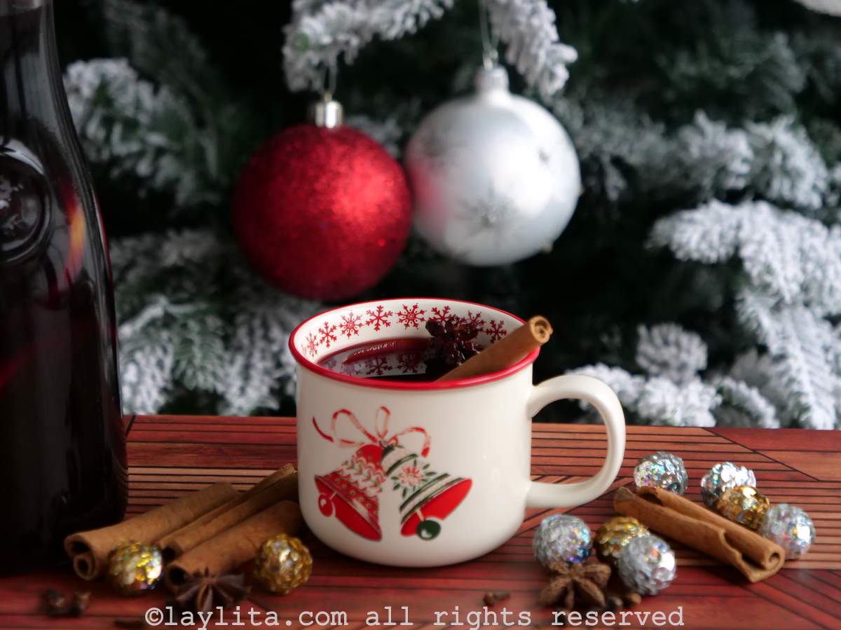 Christmas themed mug with spiced wine next to a glass jug of spiced wine and Christmas decorations