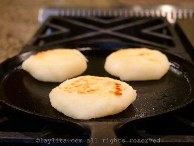 Three yuca patties cooking on a grilled