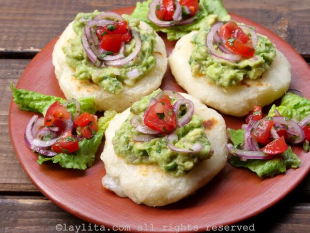 Three tortillas de yuca on a red plate, each topped with avocado and tomato and onion salad.