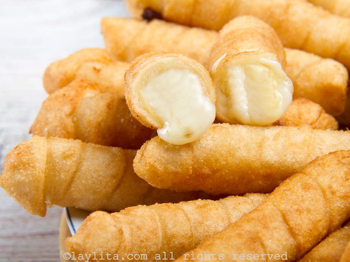 Platter of crispy cheese tequeños with one broken in half to show the cheesy center