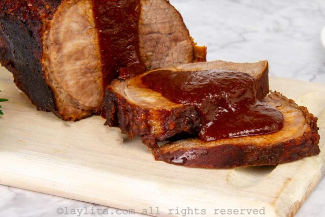 Venezuelan Asado negro served on a wooden board with some slices off the end and a sauce on top.