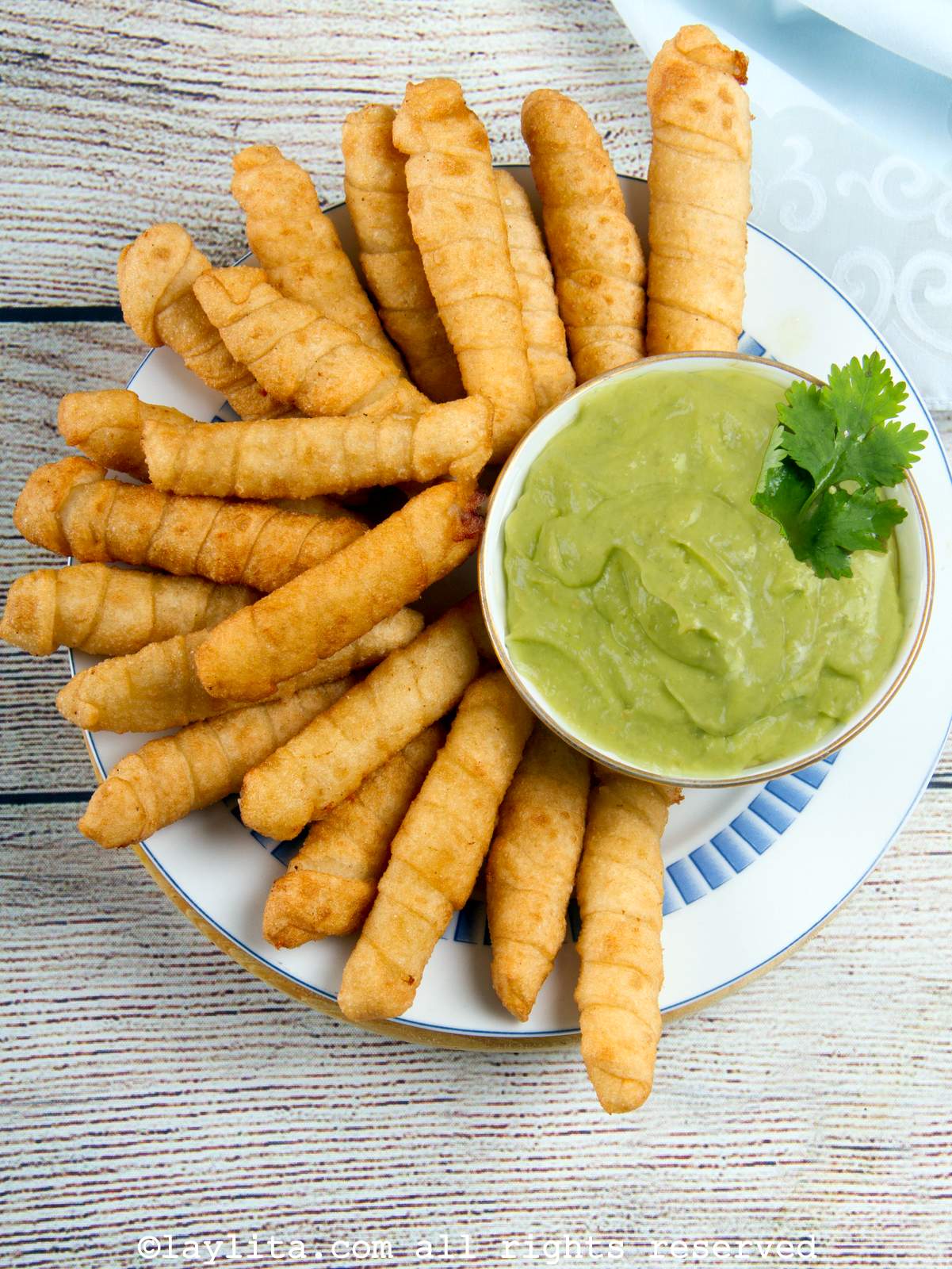 Overhead shot of a plate filled with Venezuelan cheese tequeños with a bowl of avocado sauce on the side on the palte