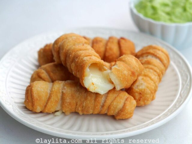 Venezuelan cheese tequeños on a white plate with one tequeño broken in half with melted cheese coming out