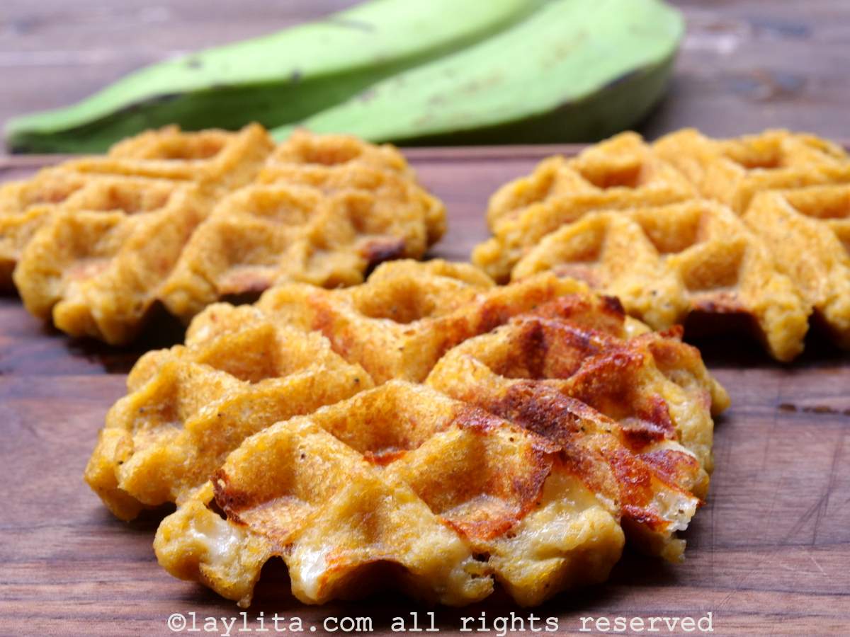 Three savory green plantain waffles on a board, one of them has cheese oozing out