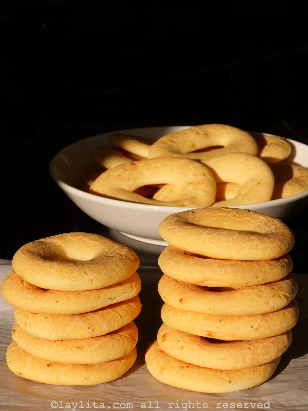 Chipa stacked on top of each other in two columns and some with a bowl with a black background behind it.