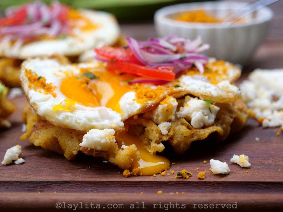 Side view of a green plantain waffle topped with an egg with a broken yolk and tomato onion salsa