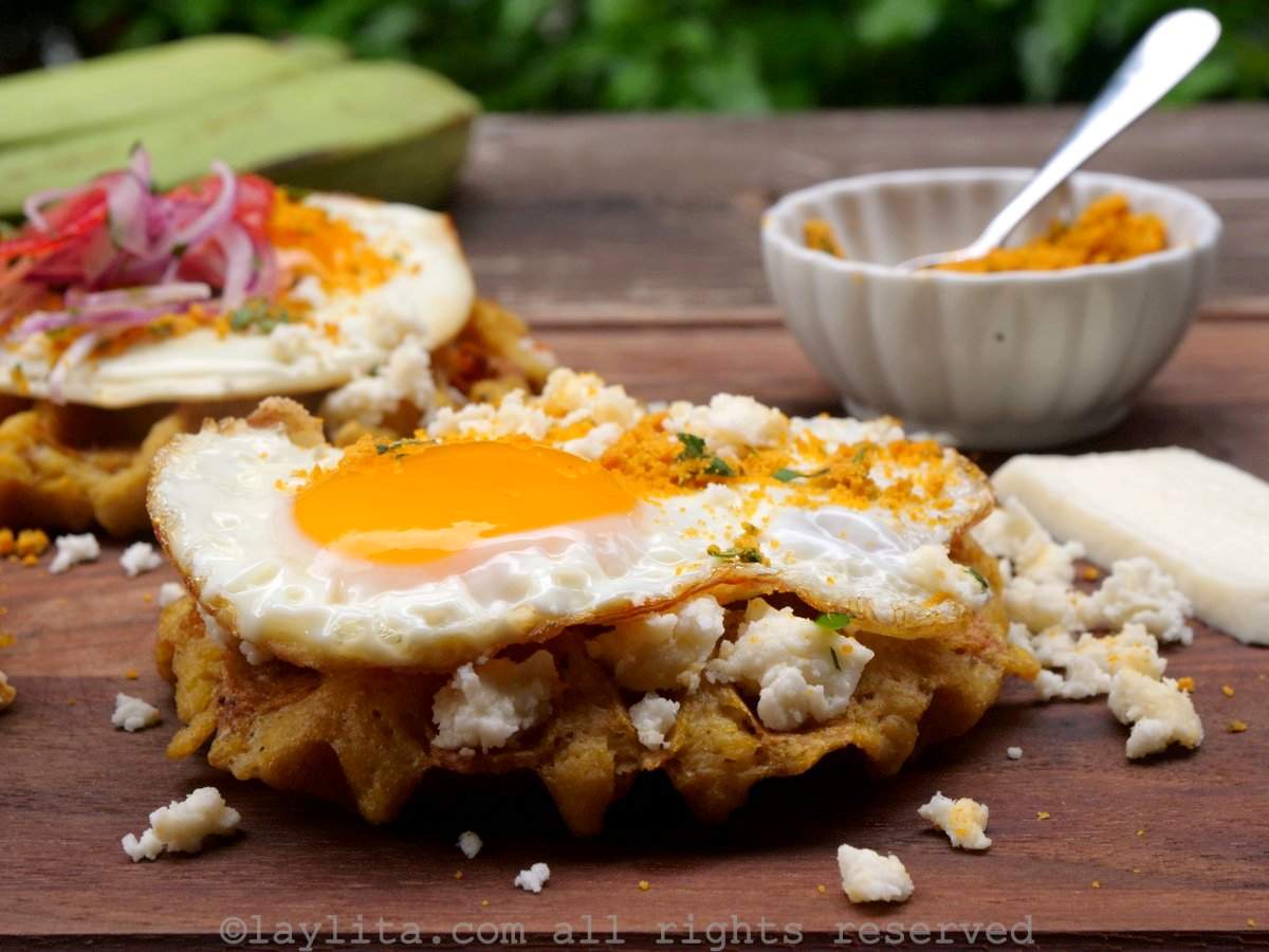 Side view of a green plantain waffle topped with cheese and a fried egg