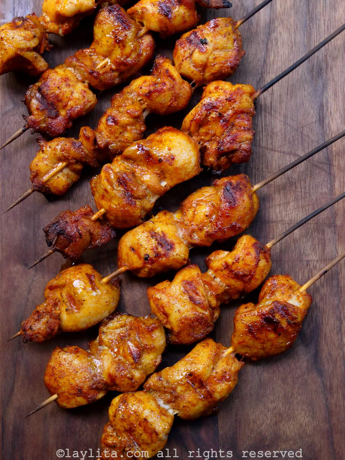 A bunch of grilled chicken skewers lined up diagonally on a wooden background