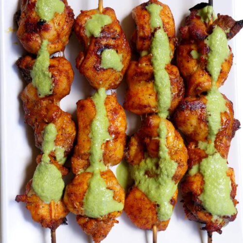 Four chicken skewers lined up with a green sauce drizzled on top.