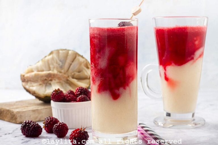 Two soursop blackberry smoothies, each in different glasses next to some fresh blackberries and an open soursop.