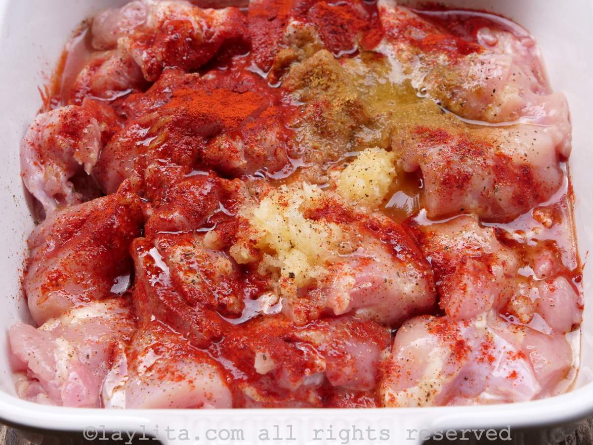 Chunks of raw chicken with achiote powder, crushed garlic, cumin and orange juice on top in a white baking pan