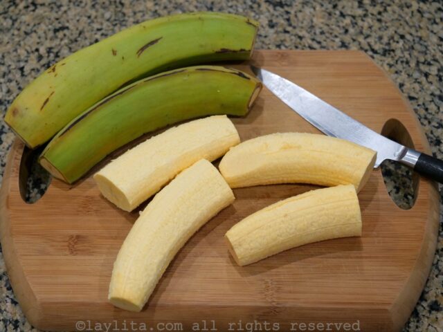 Green plantains being peeled and cut on a wooden cutting board