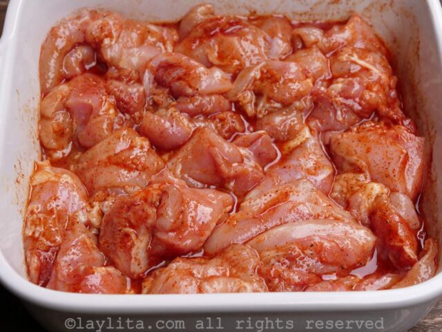Chunks of chicken marinating in a white baking pan