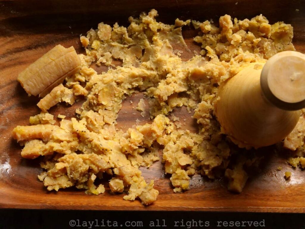 Boiled green plantains being mashed with a wood masher