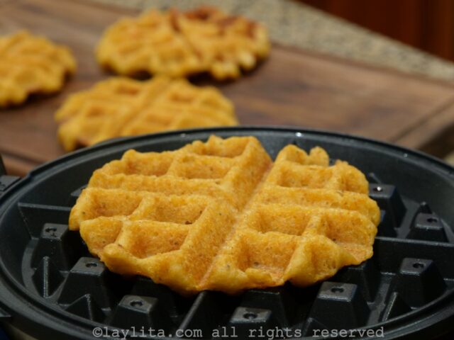 A green plantain waffle cooking a waffle maker with more in the background