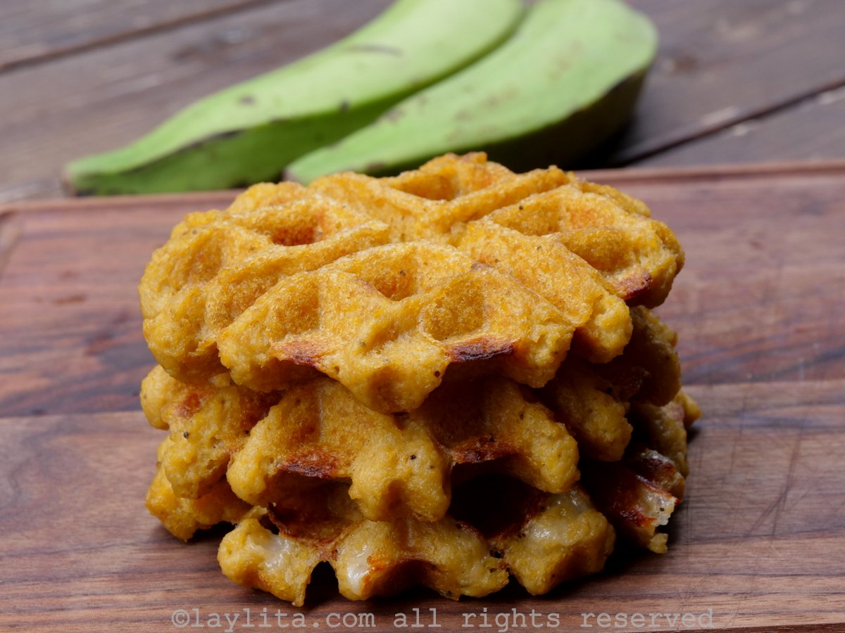 Three savory green plantain waffles stacked on top of each other on a wooden cutting board