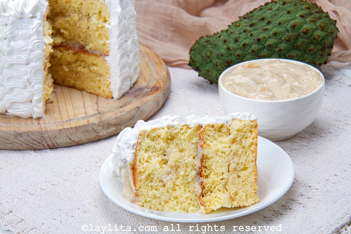 Soursop cake on a wooden board with one slice missing and placed on a plate next to it.