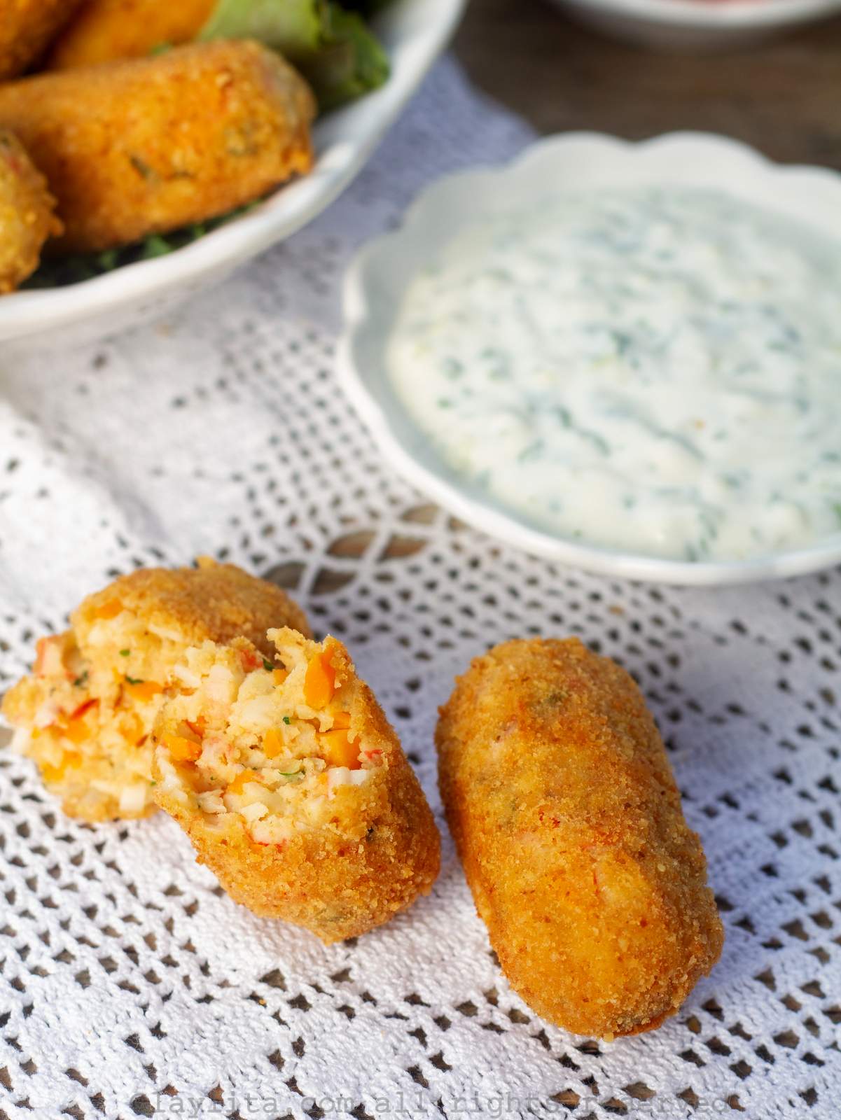 Two crab croquettes with one of them broken in half to show the inside.