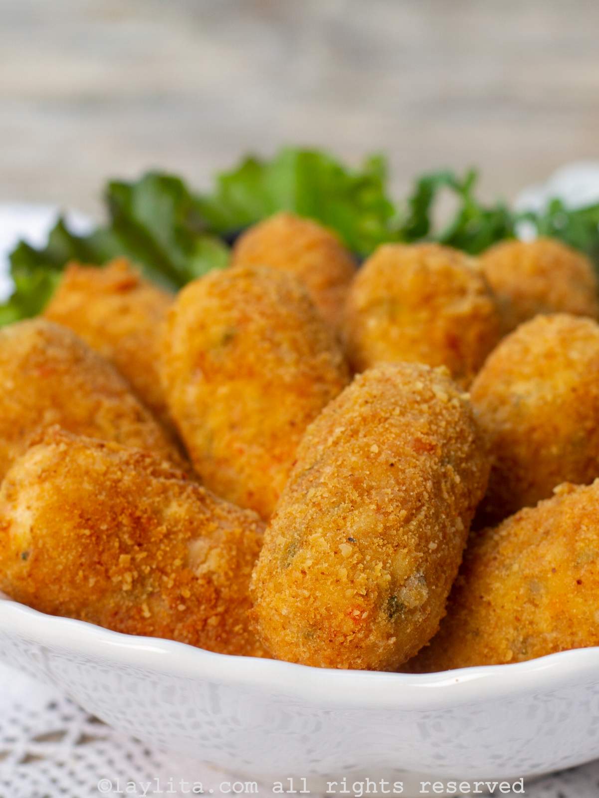 A white bowl filled with crispy oval croquettes on top of lettuce leaves