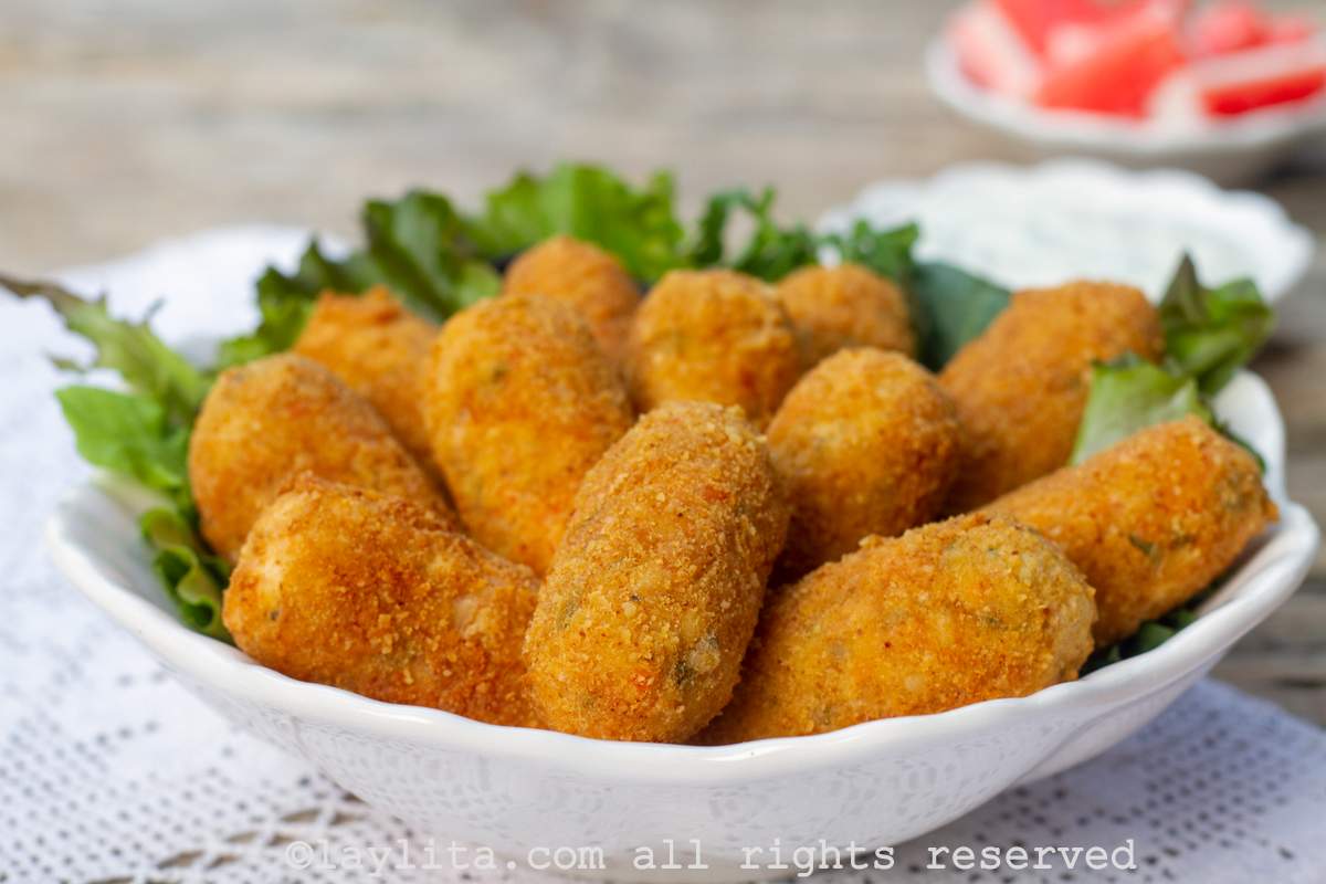 Crab croquetas in a white plate on top of lettuce leaves