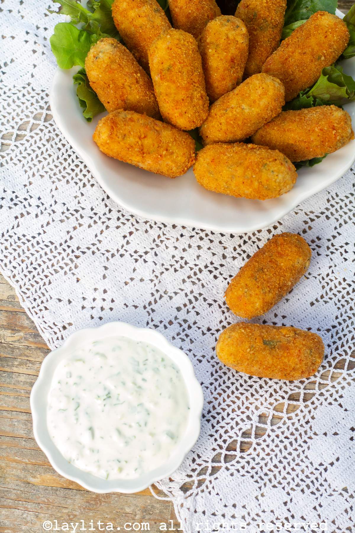 Overhead shot of crab croquettes in a white bowl with two outside the bowl next to a smaller bowl of tartar sauce