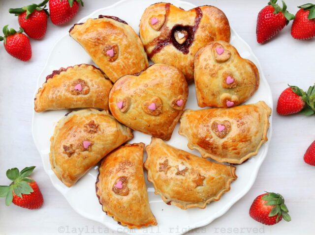 Overhead shot of strawberry chocolate empanadas on a white plate on a white background with strawberries on the sides