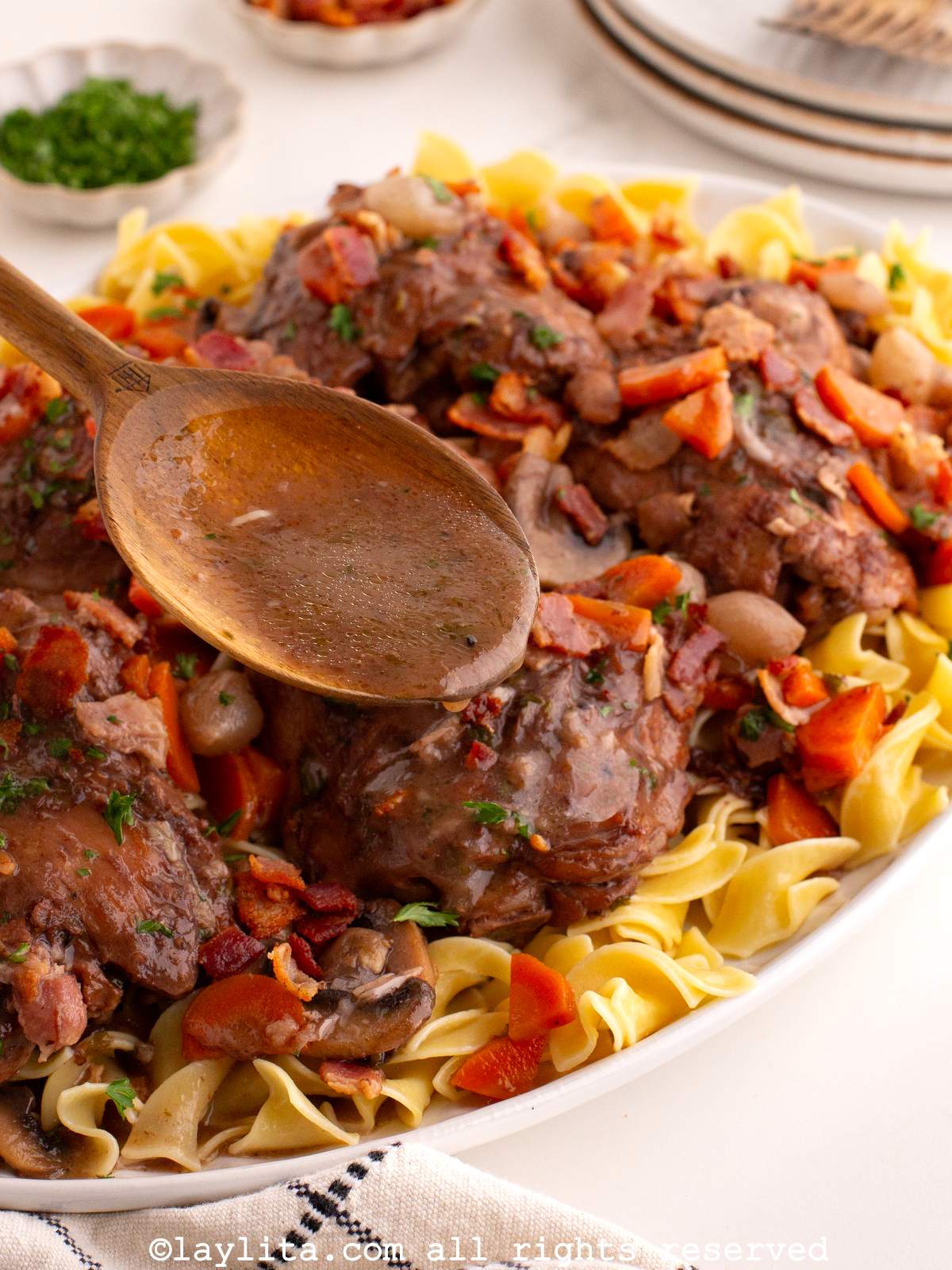Overhead view of a platter filled with coq au vin and a spoon pouring over a rich brown sauce