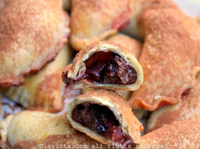 Side view of a strawberry chocolate empanada broken in half to show the inside on top of more empanadas.