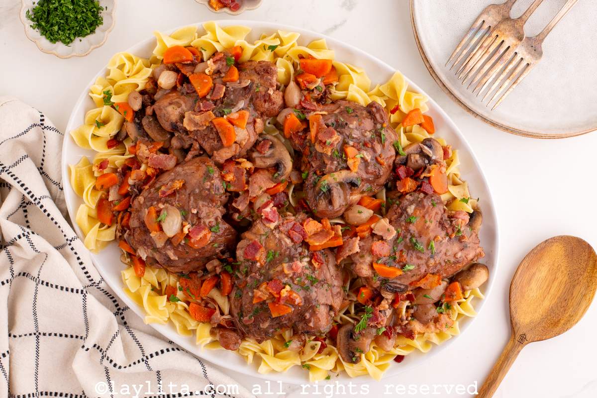 Overhead shot of  a large white platter with braised chicken thighs in red wine sauce served on top of noodles