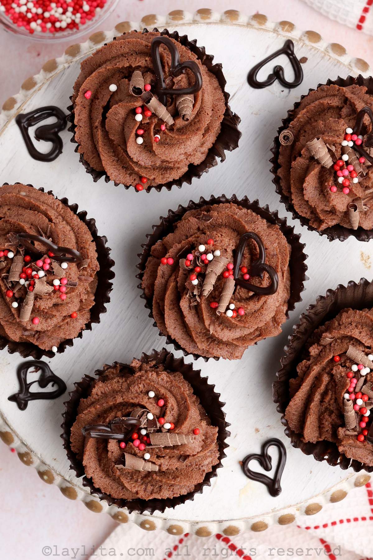 Overhead shot of several chocolate mousse cups decorated with sprinkles and chocolate hearts on a wooden plate