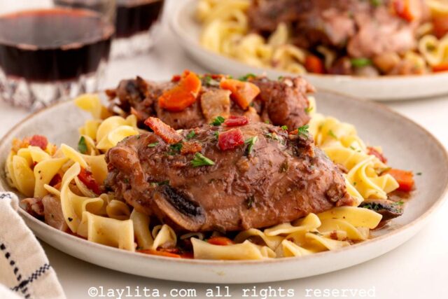 A chicken thigh served over pasta in a white plate