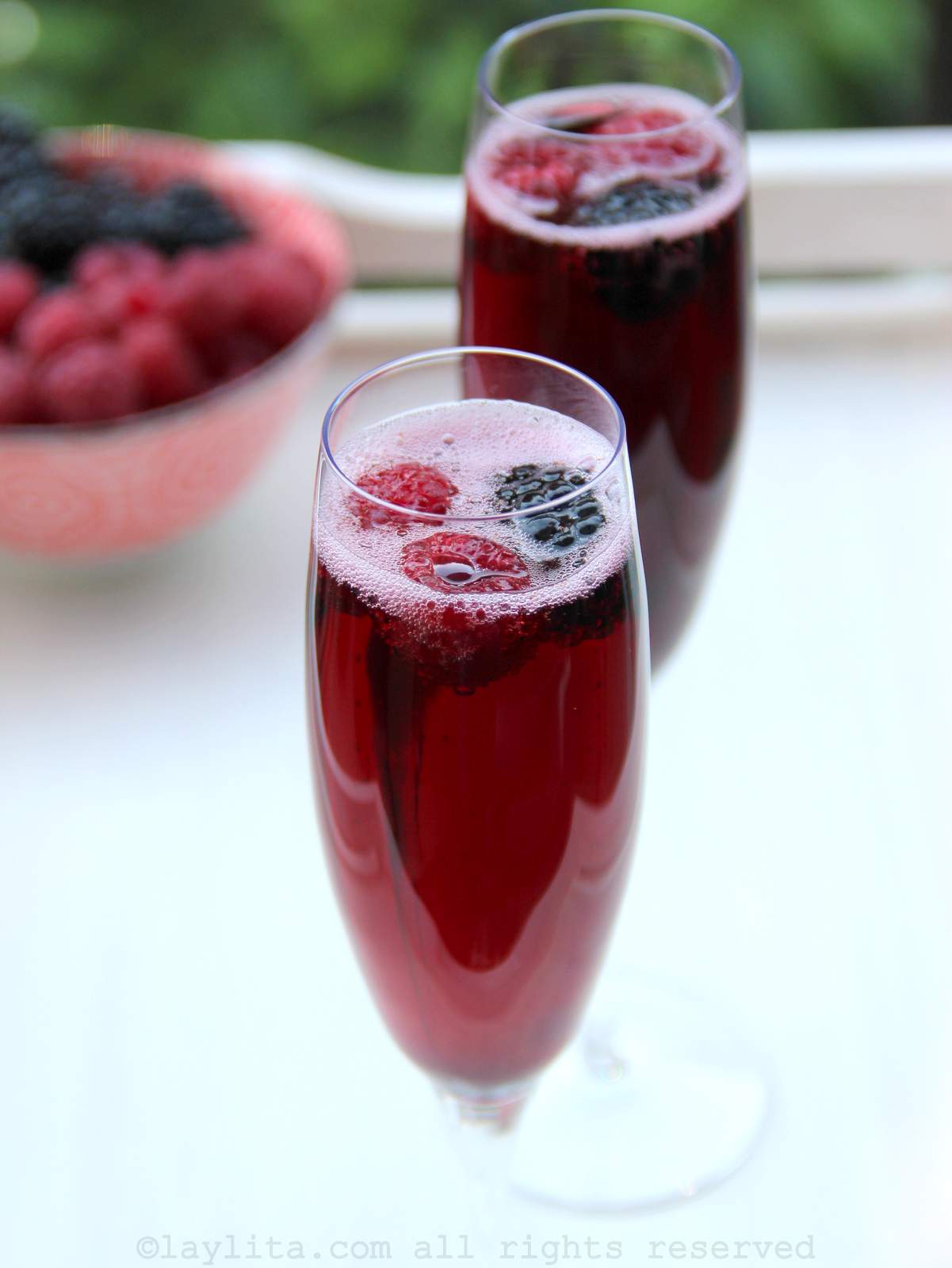 Two glasses of French Kir Royal garnished with berries and more berries in the background
