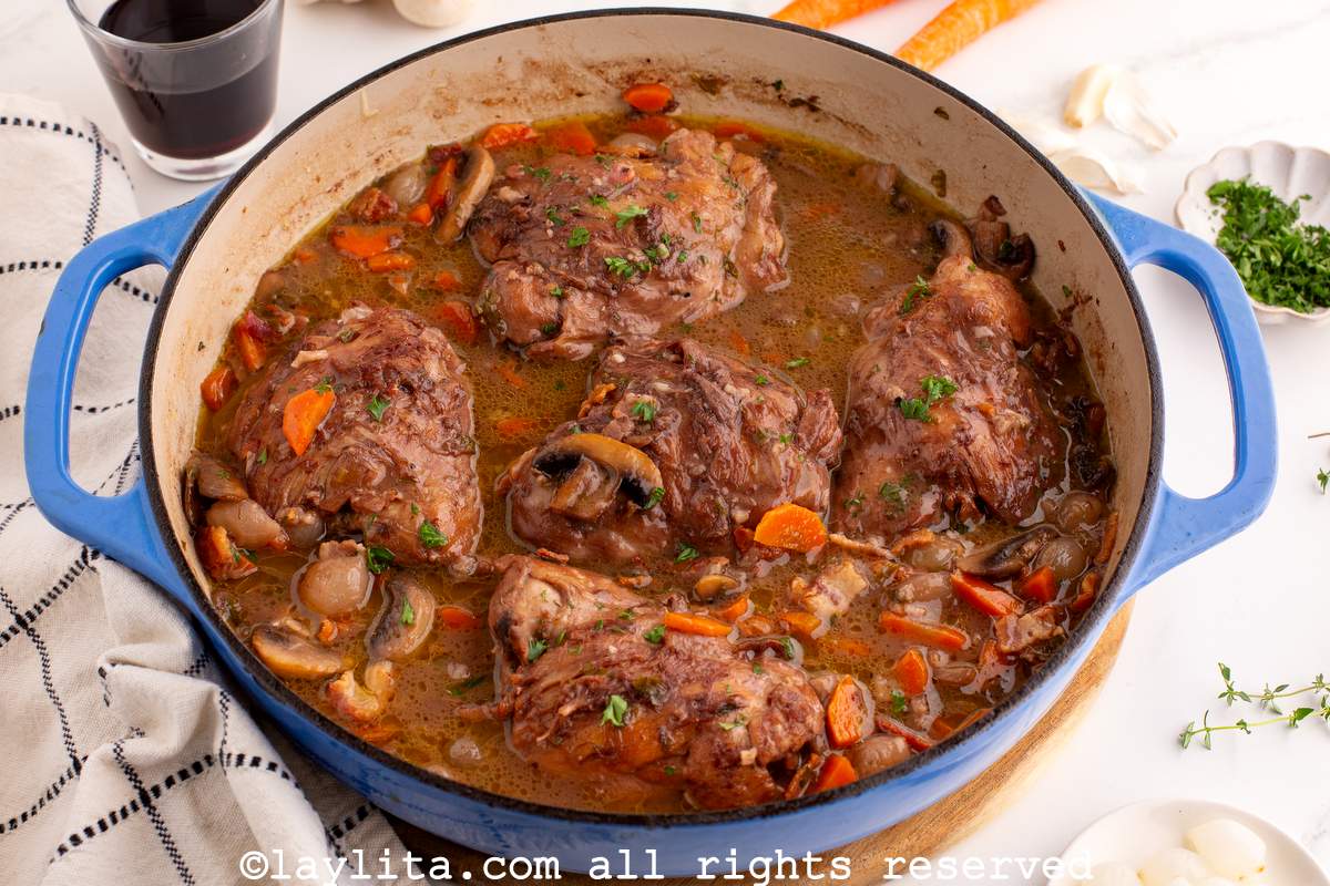 Overhead shot of a large blue ceramic pot full of chicken stew cooked in a red wine sauce with carrots and mushrooms