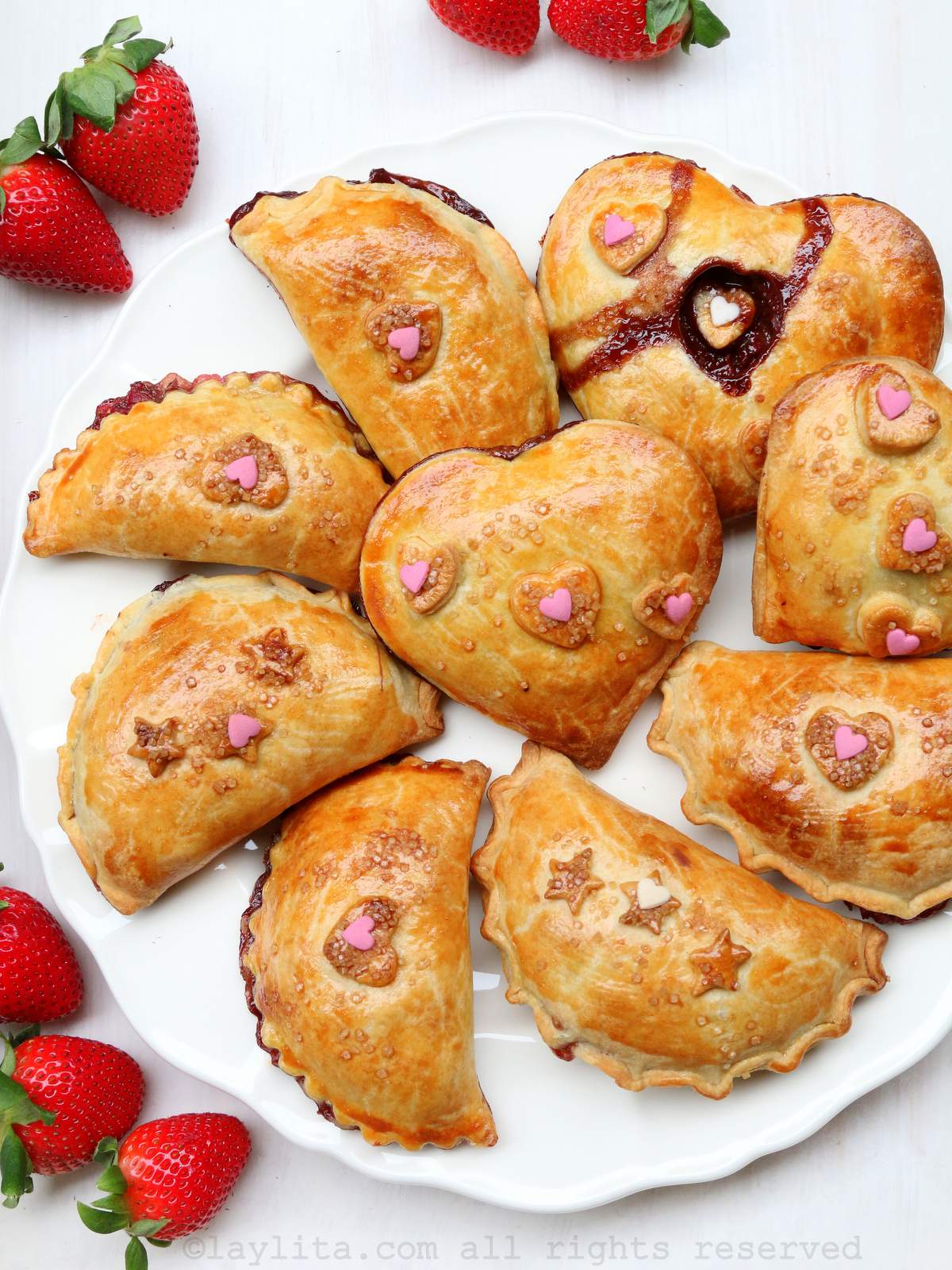 A white plate full of strawberry chocolate empanadas on white tray with some fresh strawberries on the side